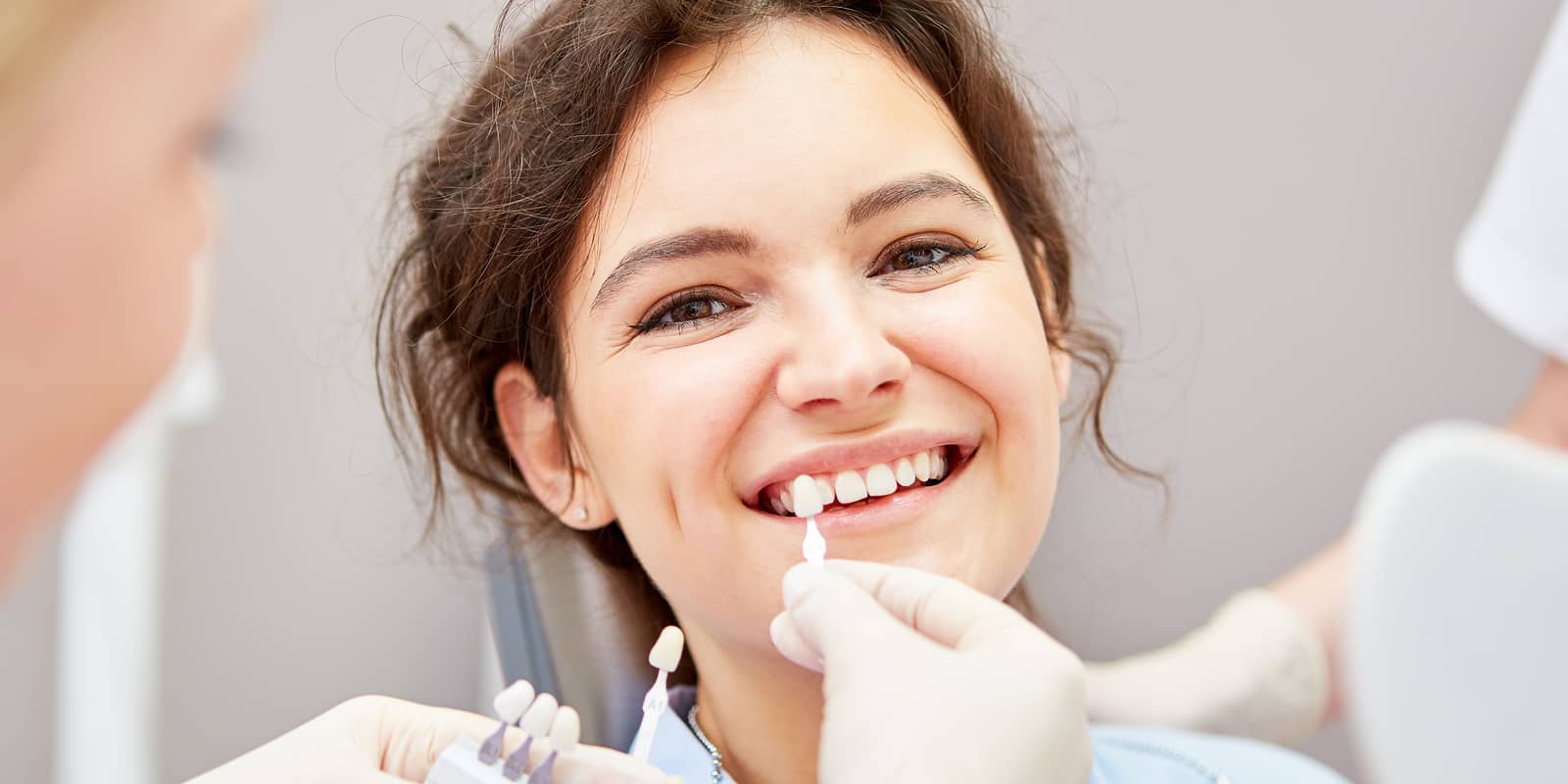 Smiling patient with dentist choosing teeth shade